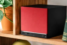 Steam Machine باللونين الأحمر والأسود على رف خشبي داخل غرفة منزلية